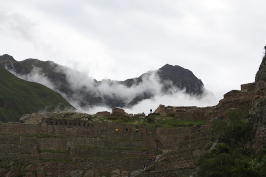 few people standing near brown castle viewing mountain under white sky in Cuzco Peru