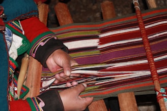 a woman is weaving a colorful blanket on a loom