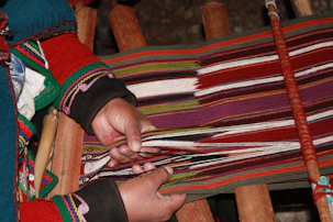 a woman is weaving a colorful blanket on a loom
