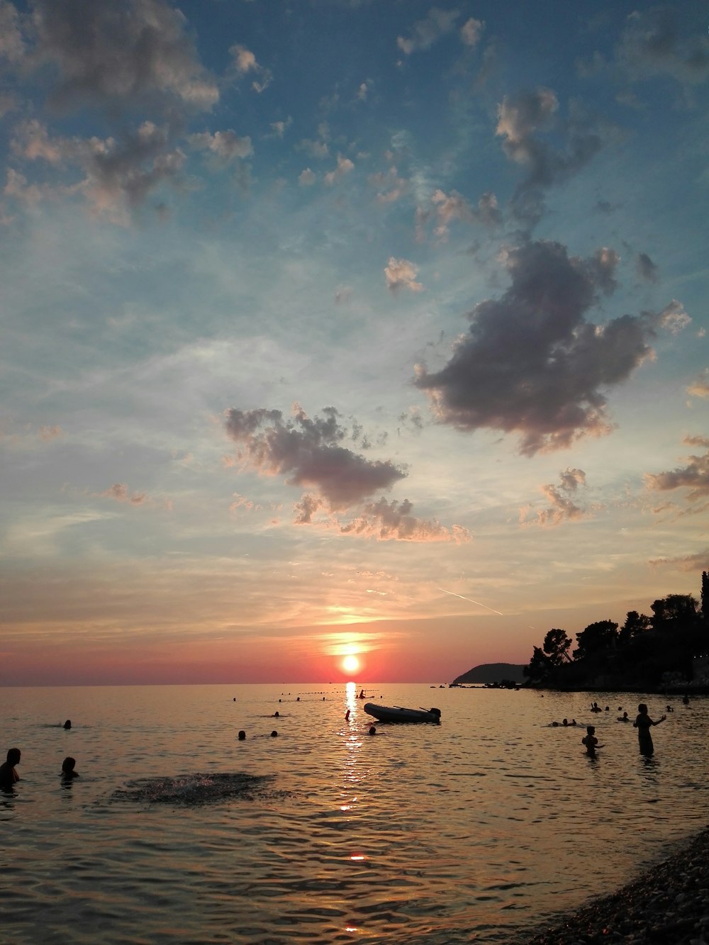 silhouette of people swimming on water under sunset