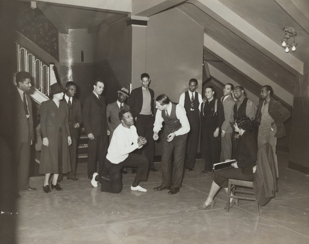 woman sitting and facing man taking a knee beside standing men and women indoors