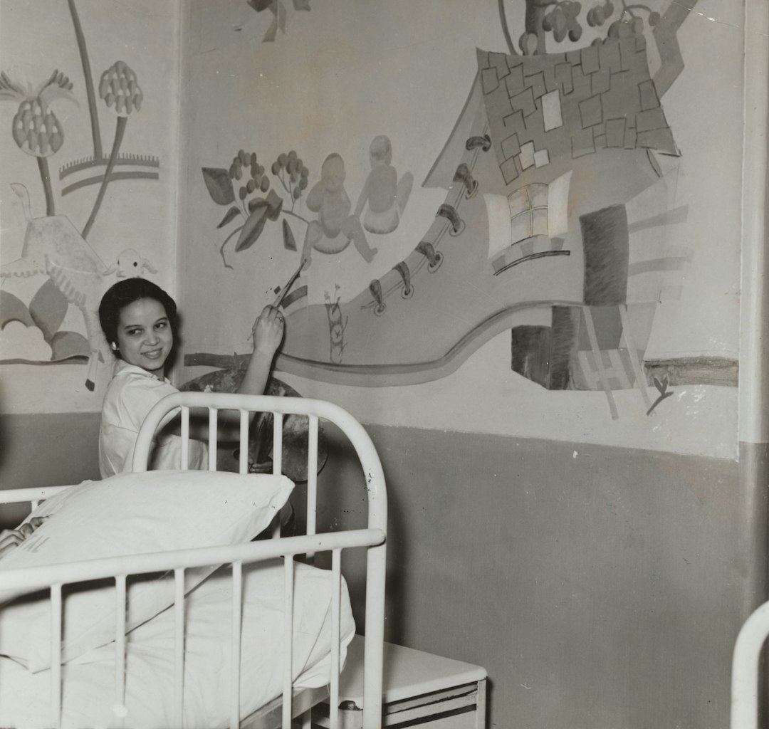 grayscale photo of woman beside steel bed frame