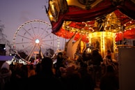 A panoramic view of the carnival grounds glowing under evening lights with happy attendees.