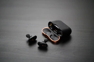 Minimalist gold-accented wireless earbuds resting on a deep navy surface.