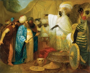 A group of elaborately dressed men gathers around a central figure pointing toward them. The setting appears rich and opulent, with intricate fabrics, gold objects, and ornate headgear. The central figure wears a white robe and a headdress with feathers, emphasizing their authority. Other figures are adorned with vibrant clothing, turbans, and accessories, suggesting a historical or cultural scene.