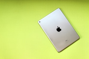 A silver iPad with the Apple logo on the back rests on a bright lime green background. The iPad is positioned diagonally, showcasing its sleek metallic design and minimalistic aesthetic.