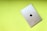 A silver iPad with the Apple logo on the back rests on a bright lime green background. The iPad is positioned diagonally, showcasing its sleek metallic design and minimalistic aesthetic.