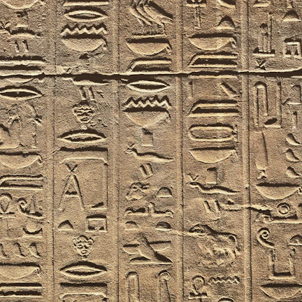 Close-up of weathered Egyptian hieroglyphs carved into a massive sandstone megalith.