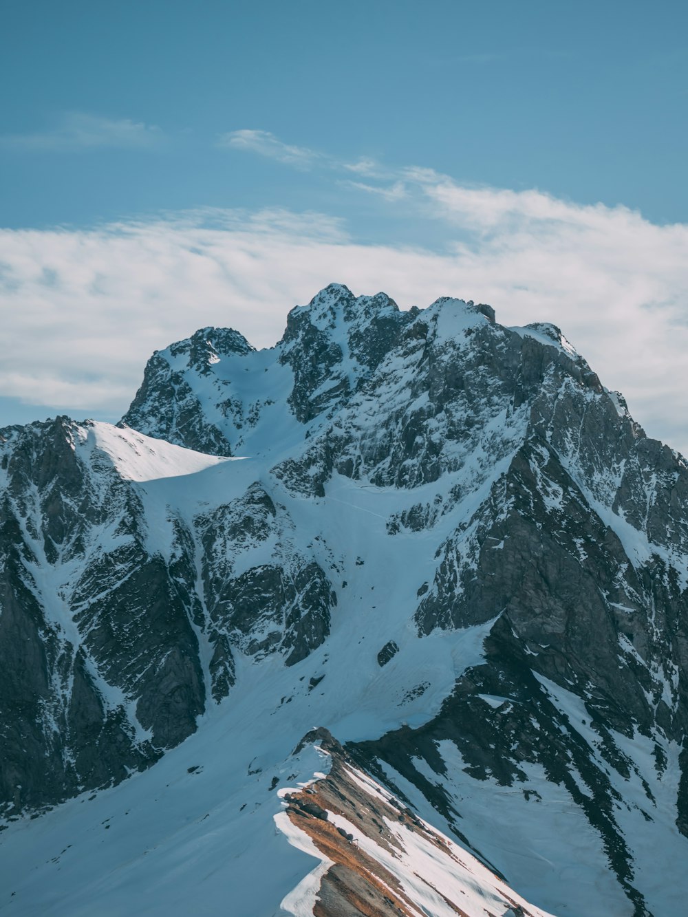 Photographie aérienne de vue du sommet d’une montagne couverte de neige sous un ciel blanc et bleu