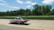A streamlined solar-powered car is driving on a road with a lush green forest backdrop. The car features a sleek aerodynamic design with solar panels on its surface and carries the number 92 along with various logos. The background is slightly blurred, suggesting high speed.