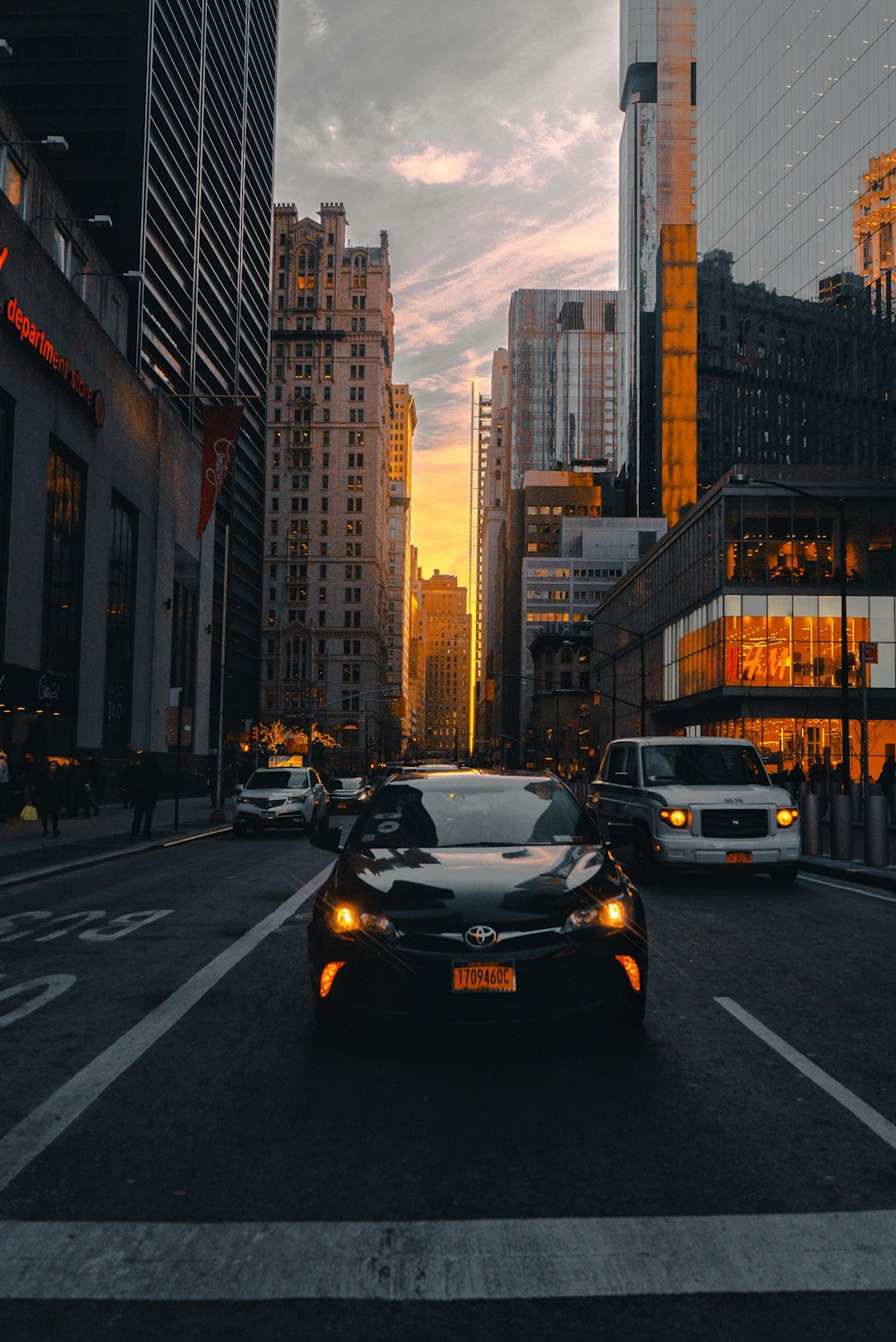 black Toyota vehicle near other vehicle on road viewing high-rise buildings under blue and white sky