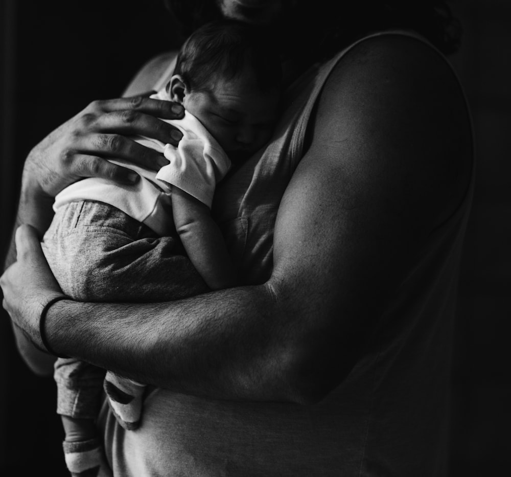 Graustufenfotografie eines Mannes, der ein Baby trägt