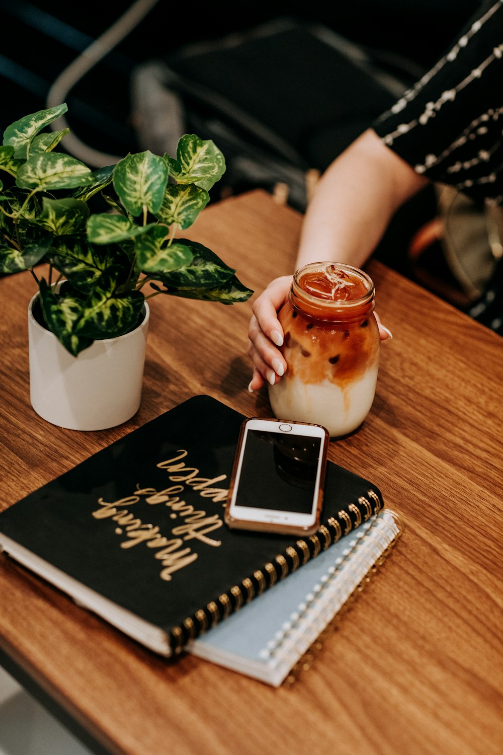 iPhone on top of a stringed notebook beside Mason jar of brown drink