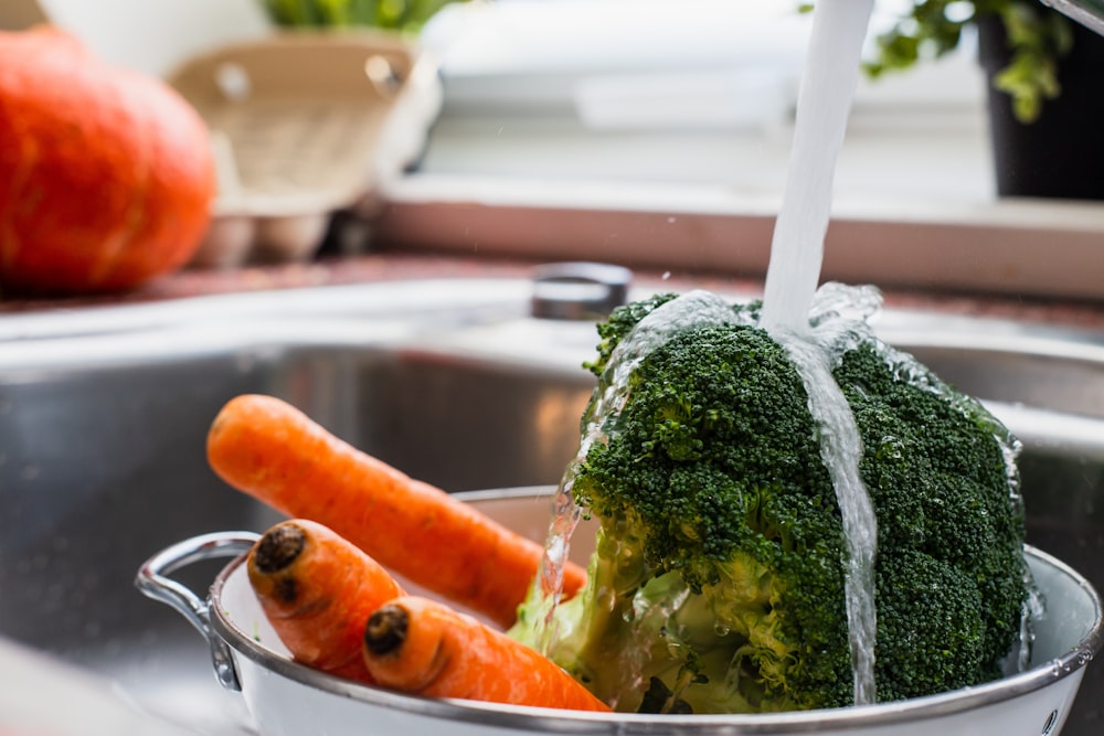 water being poured on carrots and broccoli in bowl