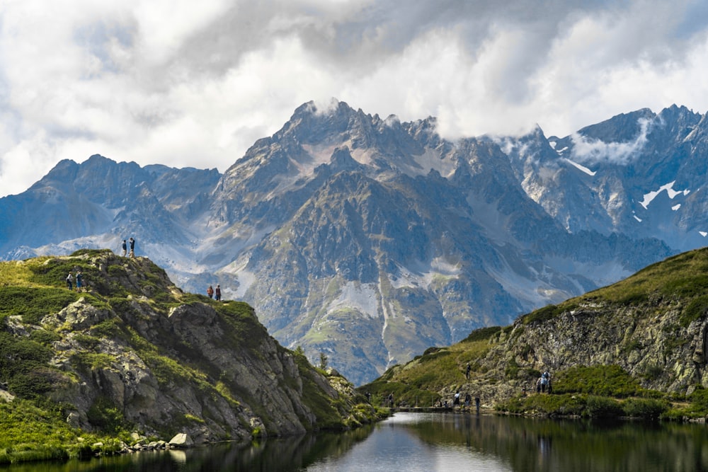 people standing on cliff viewing summit of mountain and lake under white sky