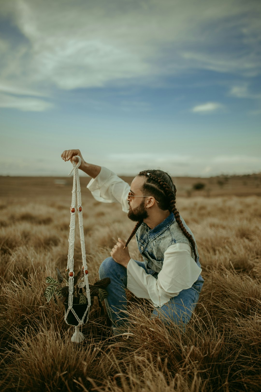 man with braided hair holds macrame hanging plant on open field