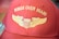 A red baseball cap features gold embroidered wings and the text 'Wings Over Miami.' The stitching includes a stylized emblem resembling a shield flanked by wings.