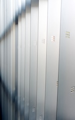 A series of metallic lockers arranged in a row, with small horizontal vents visible on each locker. The surface of the lockers reflects a soft light, creating a calm and orderly atmosphere.