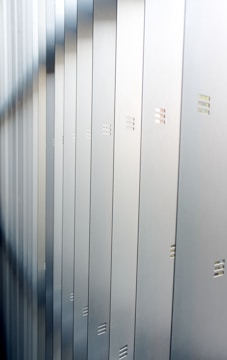A series of metallic lockers arranged in a row, with small horizontal vents visible on each locker. The surface of the lockers reflects a soft light, creating a calm and orderly atmosphere.