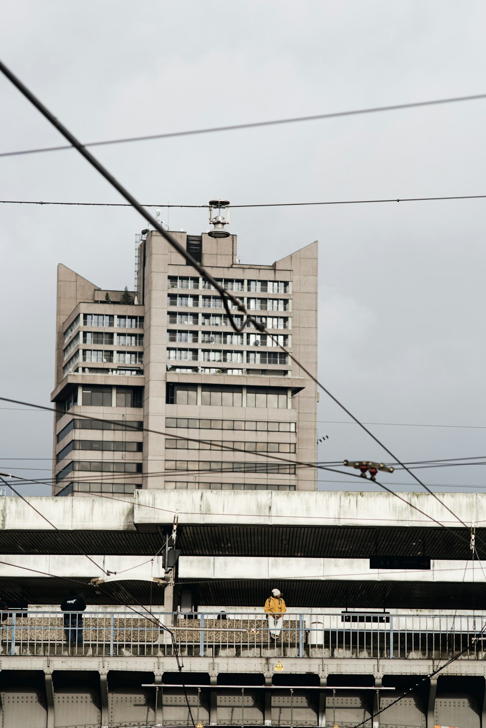 person sitting on railings near gray high-rise building under white sky