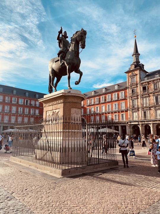man riding horse statue on pillar near people and buildings during day in Plaza Mayor Spain