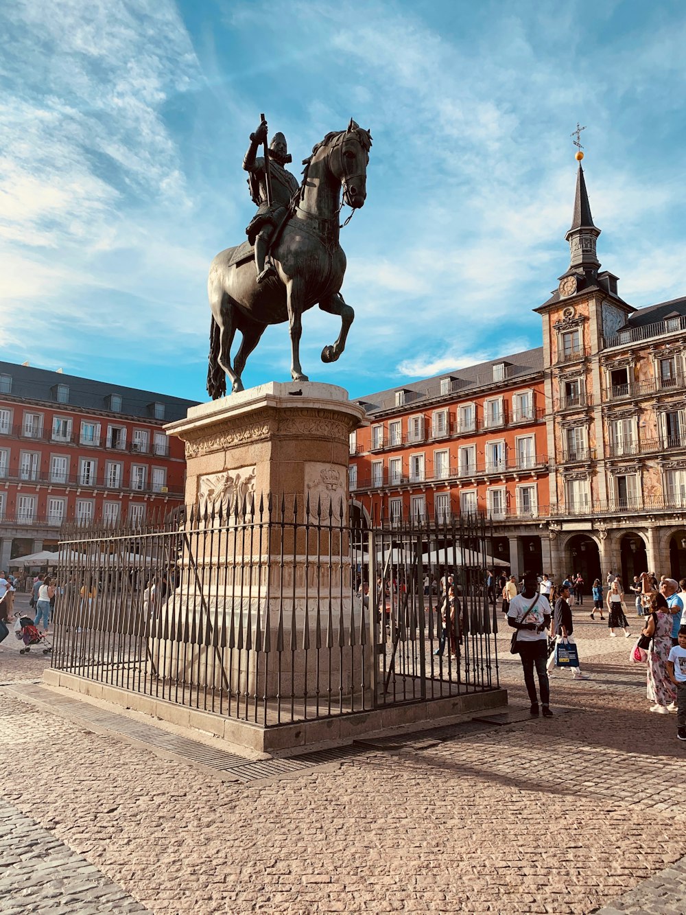 Hombre montando estatua de caballo en el pilar cerca de la gente y los edificios durante el día