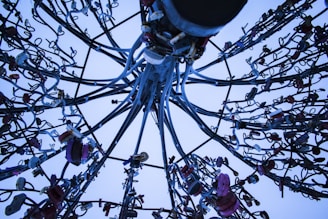 A complex array of metal cables and locks intertwined and extending in various directions, creating an intricate pattern against a pale blue sky.