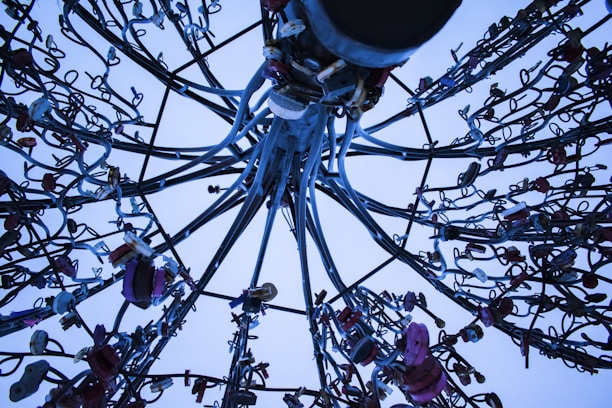 A complex array of metal cables and locks intertwined and extending in various directions, creating an intricate pattern against a pale blue sky.
