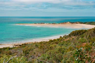 A panoramic view of a turquoise ocean meeting a white sandy beach at sunset.