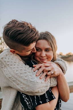 the ring,how to photograph engagement, engaged, ring, hands, couple, in love, sweater, girl meets boy, proposal, florida, usa, marriage, young adults, candles, light, rose petals, happy, cute; man hugging woman by her back during day