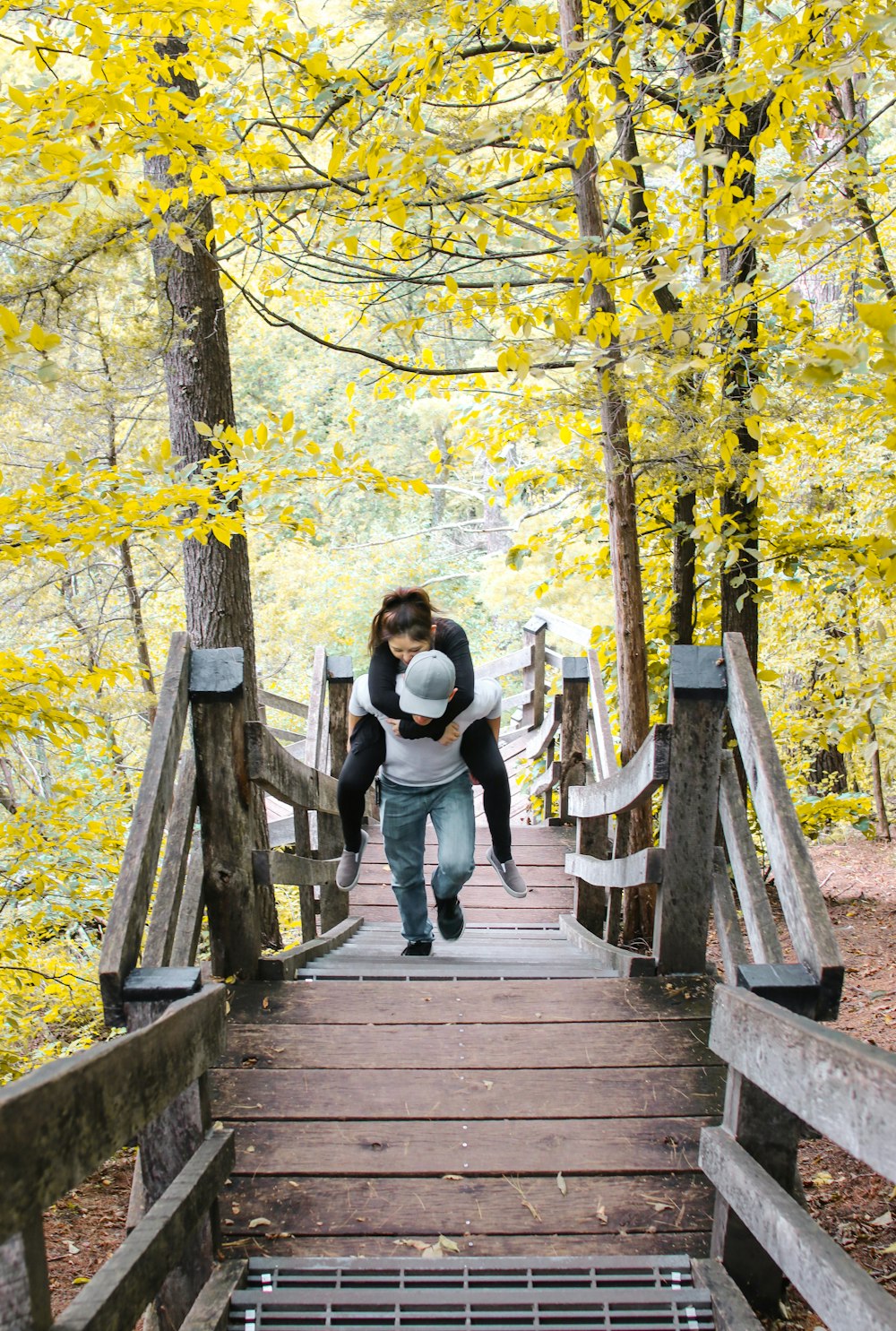 woman riding on man's back walking up the stairs near trees during day