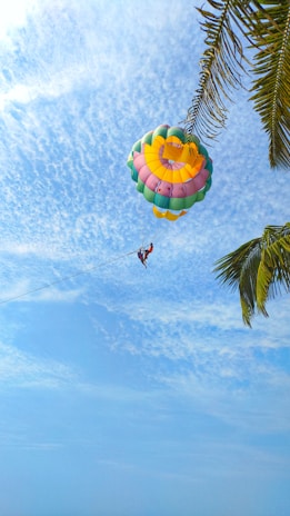 A person parasailing high above the ocean, with colorful sails against a clear blue sky.