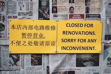 A yellow sign with black text is pinned against a wall covered in newspapers. The sign contains both Chinese and English text, with the Chinese on the left side and the English on the right, stating the establishment is closed for renovations. The newspapers in the background feature various articles and images.