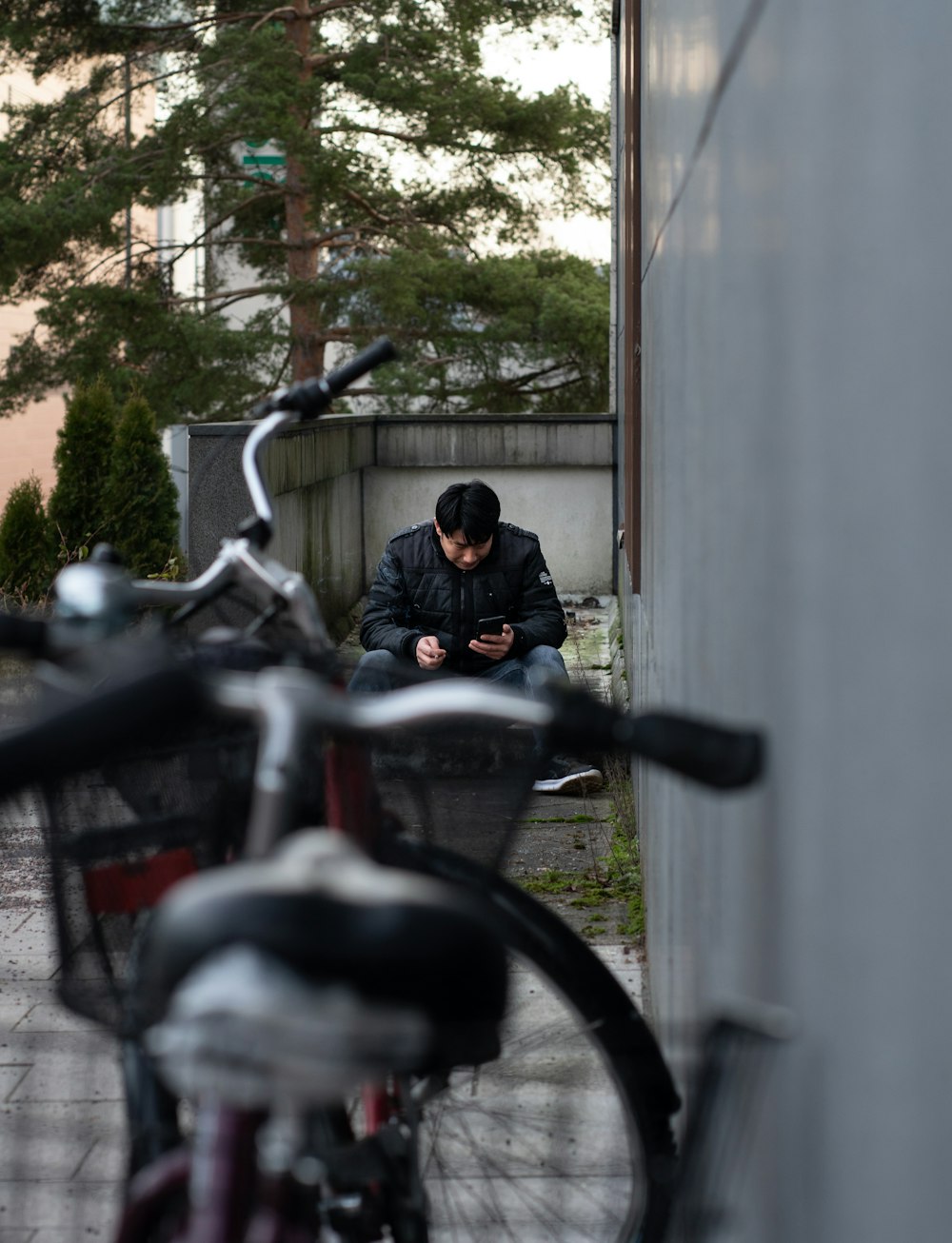 selective focus photography of man sitting near parked bike beside wall