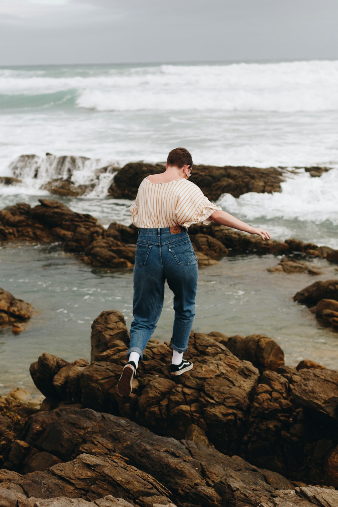shallow focus photo of person in blue denim pants in front of ocean during daytime