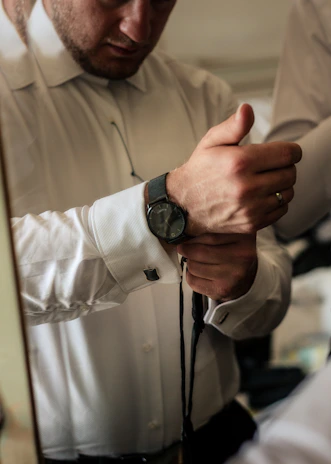 A black-and-white cinematic frame showing a groom adjusting his tie before the ceremony.