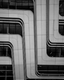 A modern architectural facade features sleek, overlapping panels with smooth, curved lines. The surface appears metallic and is dotted with small rivets, contributing to a futuristic look. Reflective glass sections are visible, partially revealing the building's interior.