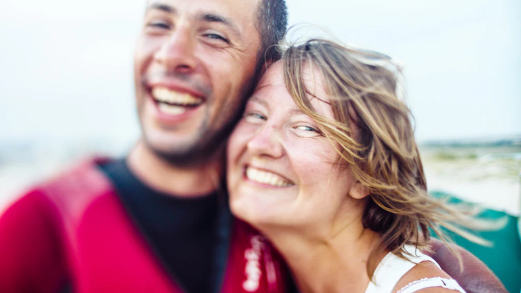 A warm, candid photo of an Asian woman and Caucasian man sharing a genuine smile outdoors, symbolizing connection.