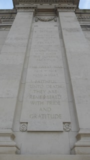 A stone memorial wall displays a dedication to the heroic sons of Belfast who sacrificed their lives in the Great War and World War II. The text is engraved in a formal, centering format. Decorative elements include carved floral designs at the top and bottom of the plaque.