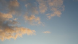 Soft, fluffy clouds with a warm golden hue are scattered across a clear blue sky.