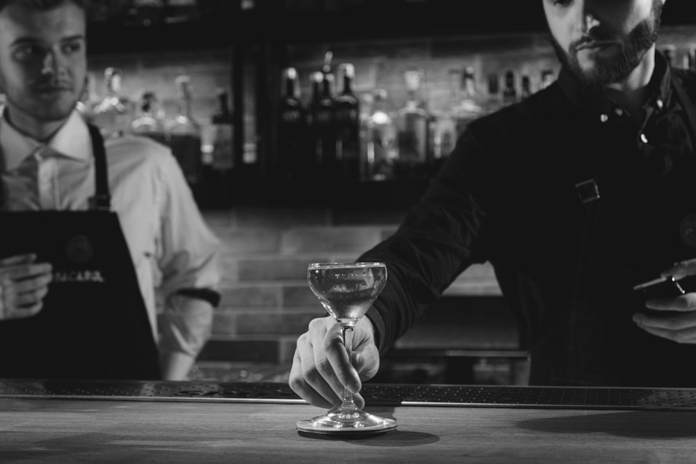monochrome photo of bartender puts glass of cocktail on top of the bar table
