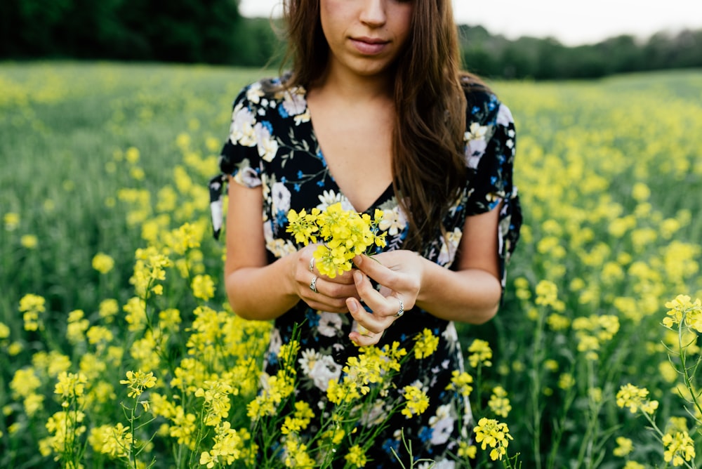 노란색 꽃을 들고 파란색, 흰색, 검은색 꽃무늬 V넥 드레스를 입은 여자