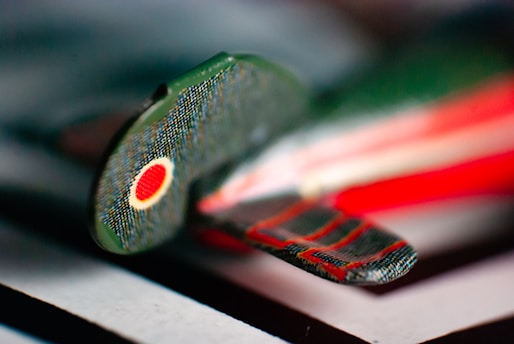 A close-up of a miniature airplane model, featuring a camouflage pattern with a red and yellow circular emblem on the wing. The background is out of focus, highlighting the details of the airplane’s surface.