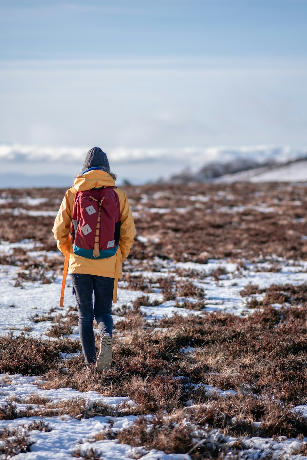 person in yellow jacket carrying red backpack while walking on snow-covered field