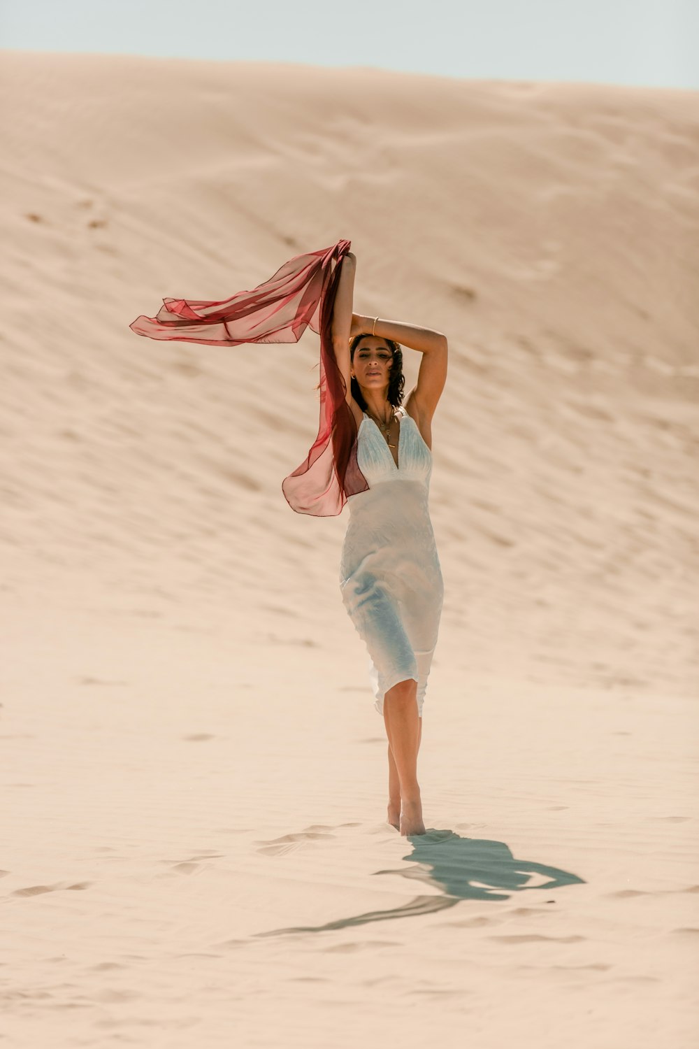 barefooted woman wearing white bodycon dress raising right hand while standing on desert during daytime