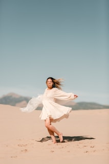 A carefree woman dancing barefoot on a beach at sunset, adorned in colorful boho clothing and feather earrings.