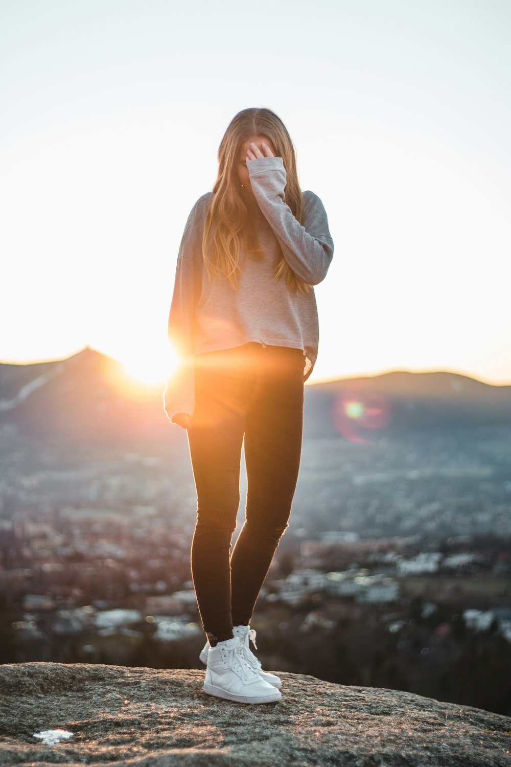 Donna che indossa una giacca grigia in piedi mentre copre il viso usando la mano sinistra