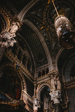 Ornate vaulted ceiling with gold detailing and a hanging chandelier in a church
