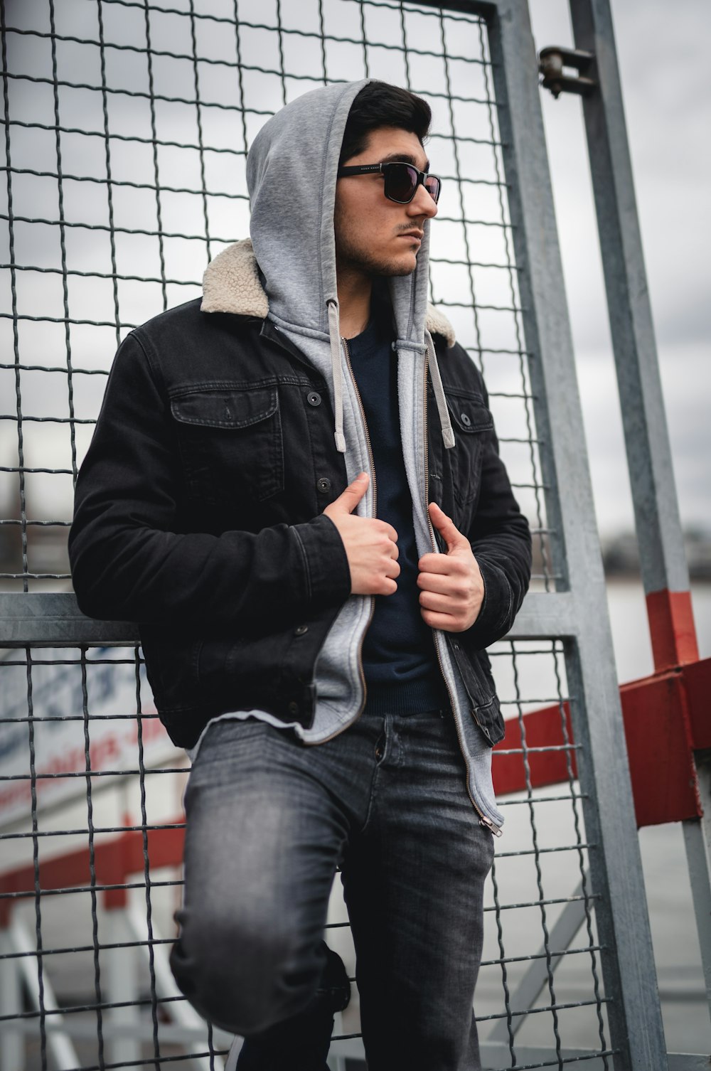 man wearing hoodie leaning on gray metal gate