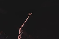 person wearing brown long-sleeved shirt raising right hand while standing
